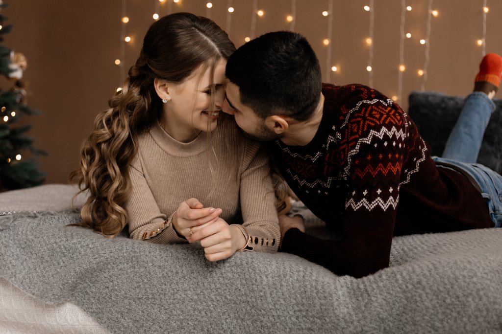family-portrait-man-and-woman-relax-on-soft-grey-bad-in-a-room-with-christmas-tree.jpg